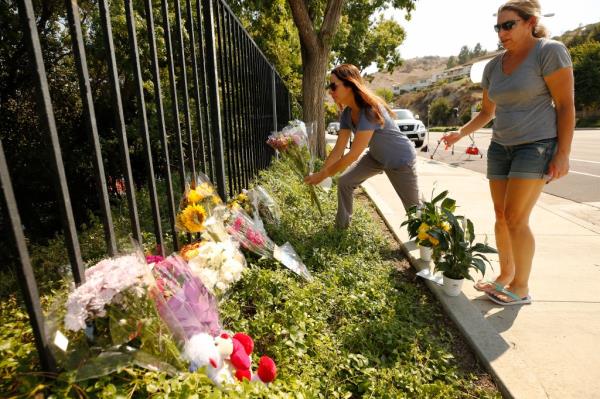 Two women in tears place flowers at a growing memorial for two brothers who were fatally injured while crossing  Triunfo Canyon Road at Saddle Mountain Drive in their Westlake Village neighborhood on Sept. 30, 2020.