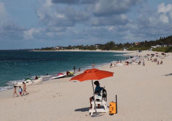 A lifeguard sits under the umbrella while watching people enjoy Paradise island beach, Nassau